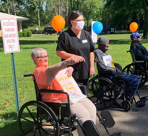 Elderly individuals participated in an outdoor event, enjoying the company of caregivers and each other while celebrating with signs and balloons.