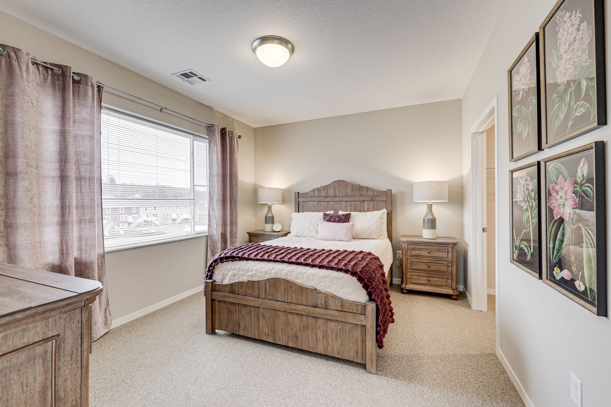 A cozy bedroom with a large window, featuring a bed with a plaid blanket and matching nightstands with lamps.