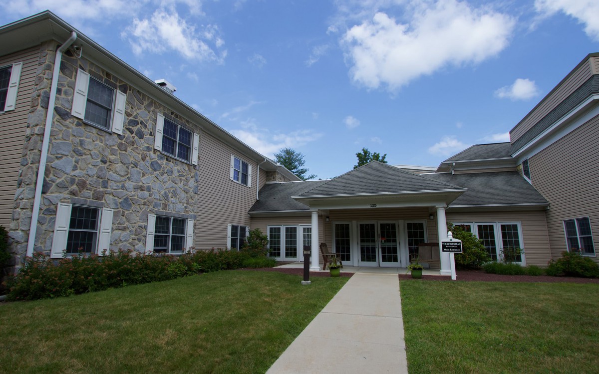A two-story residential building with a stone facade and a covered entrance under a partly cloudy sky.