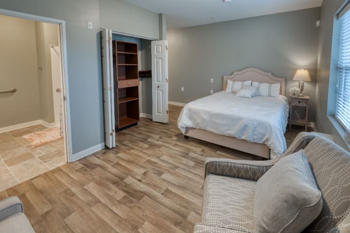A cozy bedroom with neutral colors, featuring a bed, chair, and an open closet.
