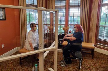 Two people sit across from each other with a transparent barrier between them.