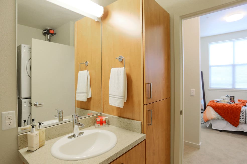 A clean and modern bathroom with a wooden cabinet, sink, mirror, and towels.