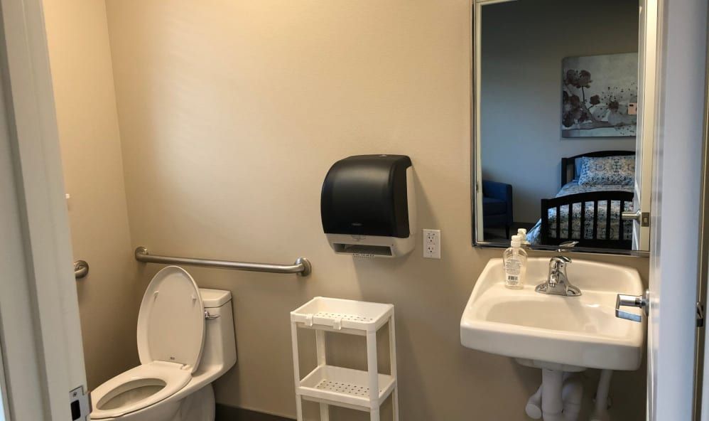 A clean, accessible bathroom with a sink, toilet, and mirror.