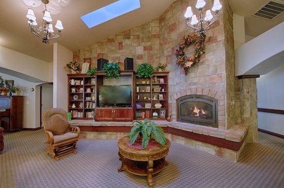 A cozy living room featuring a stone fireplace, bookshelves, and a comfortable seating area under a skylight.
