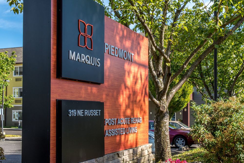 A modern outdoor sign for Marquis Piedmont, partially shaded by a nearby tree.