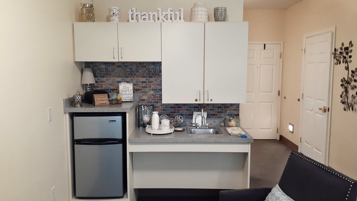 A modern kitchenette with a mini fridge, cabinets, and decorative elements on the countertop.
