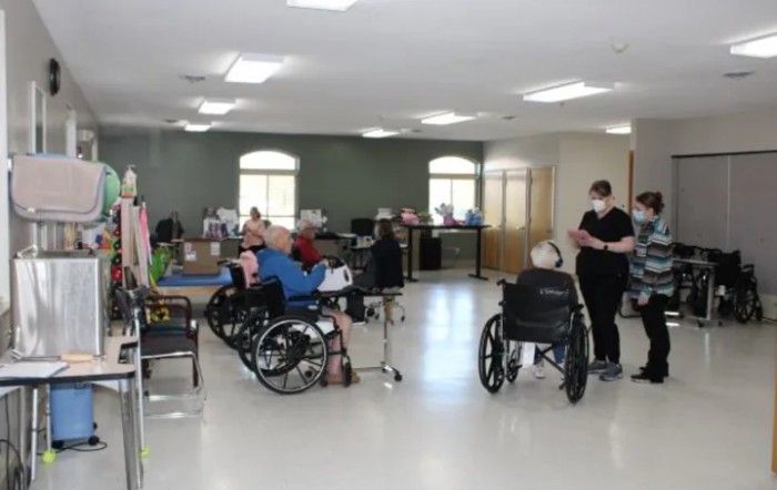 Elderly residents in wheelchairs being attended to by a caretaker in a nursing home.