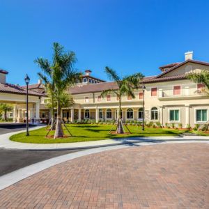 A sunny day view of a large building surrounded by palm trees and landscaped grounds.