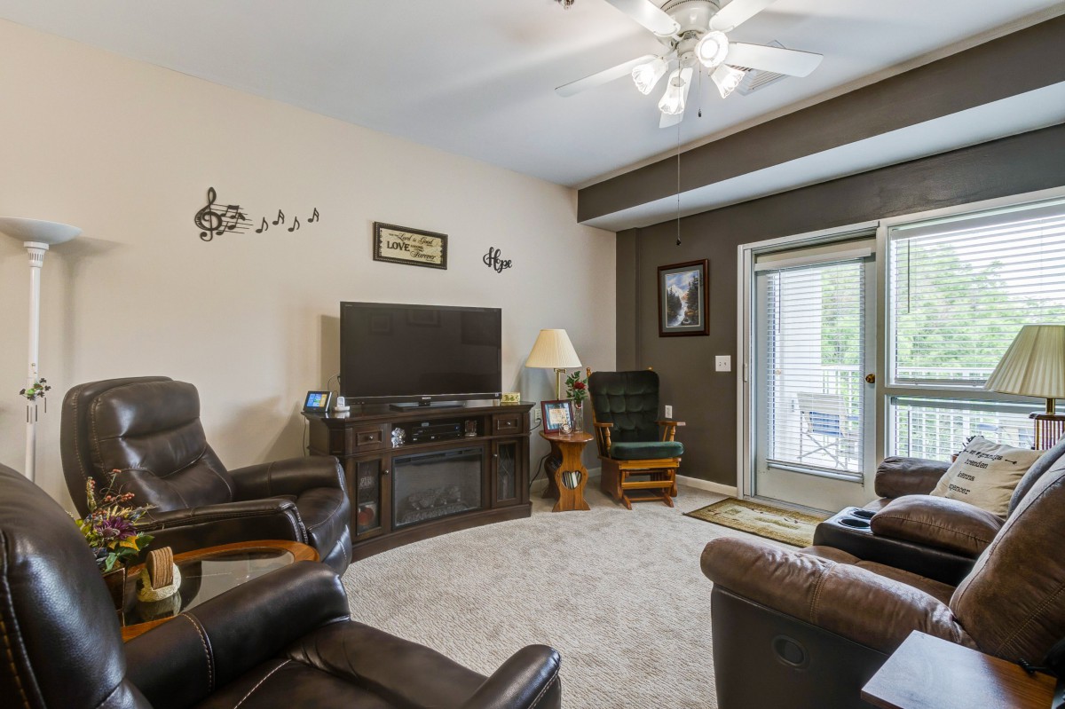 A cozy living room with comfortable seating and a large TV, featuring a ceiling fan and stylish decor.