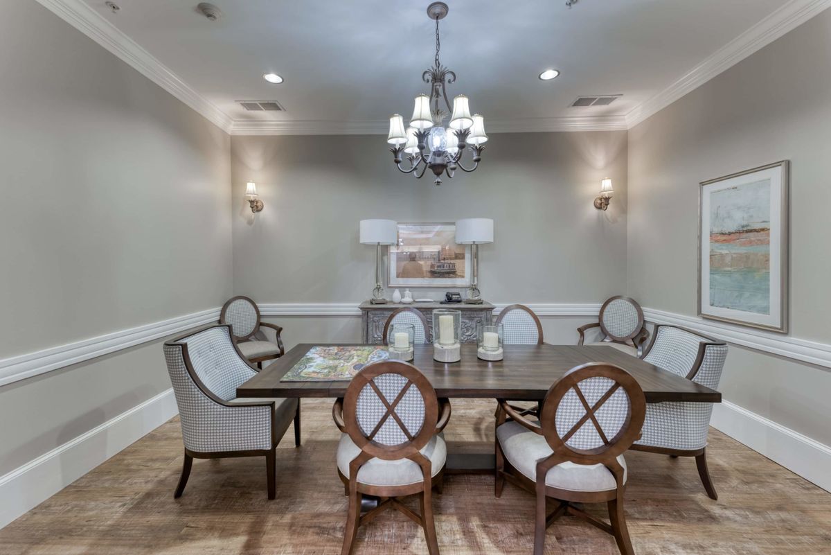 An elegant dining room featuring a central chandelier, a wooden dining table with cushioned chairs, and wall sconces for lighting.