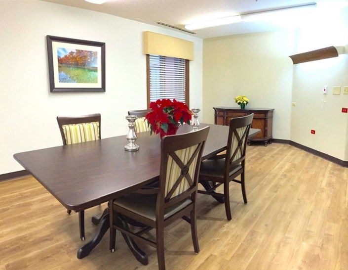 A dining room with a table set for four, featuring a vase of red flowers and artwork on the wall.