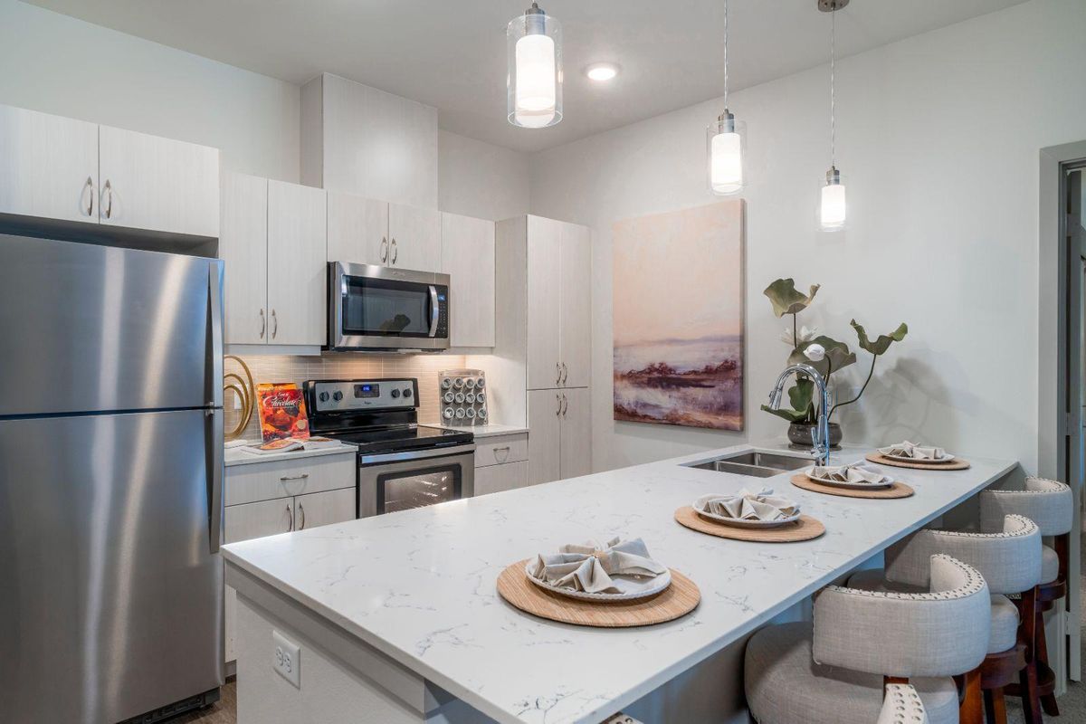 A modern kitchen with a sleek design featuring stainless steel appliances, an island with place settings, and contemporary lighting.