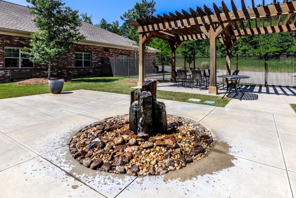 A tranquil outdoor patio featuring a fountain surrounded by rocks and a wooden pergola with seating.