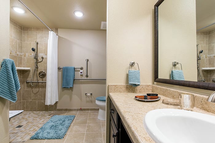 A modern bathroom featuring a spacious shower area with a curtain, a sink with a vanity and mirror, and coordinated blue towels.