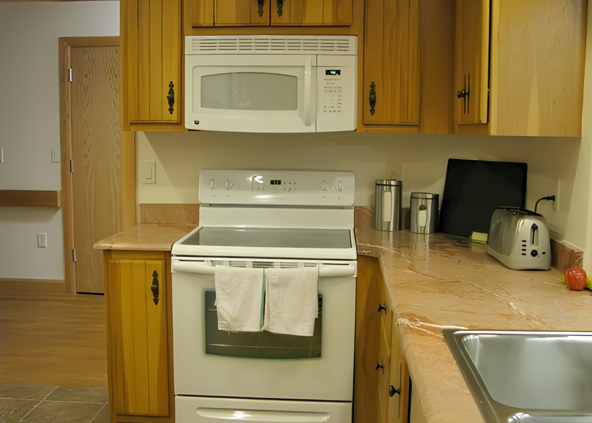 A kitchen with wooden cabinets featuring a white stove and microwave.