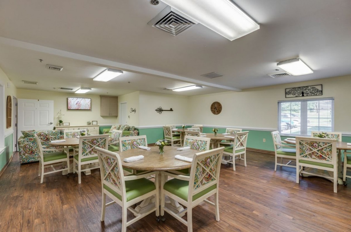 A neatly arranged dining area with tables and chairs, featuring wooden flooring and bright overhead lighting.