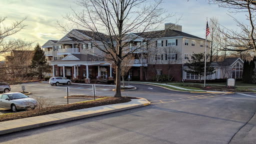 A scenic view of a residential building during sunset, featuring a tree in the foreground and a parking area.