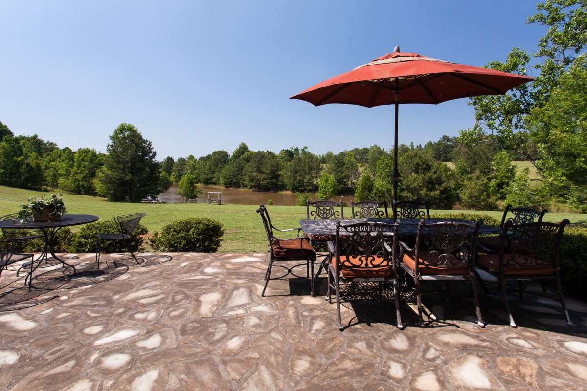 A sunny outdoor patio area with a dining set and umbrella, overlooking a lush garden landscape.