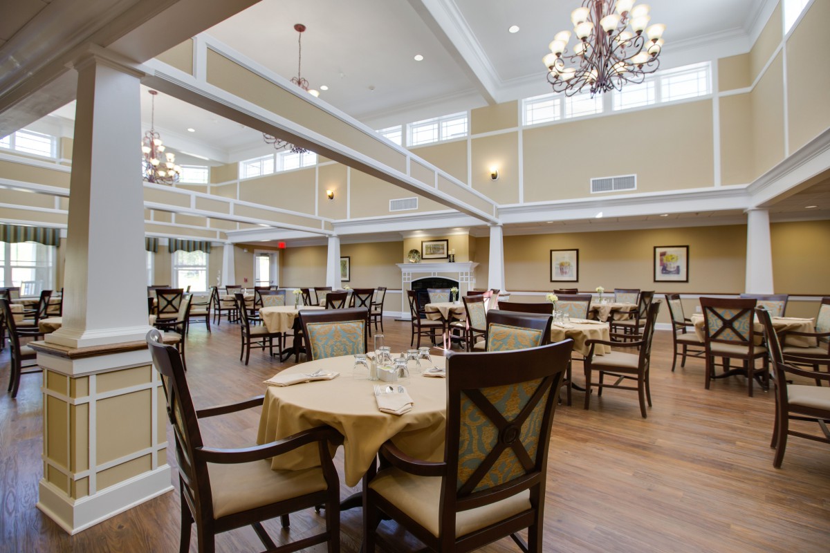 An elegant and spacious dining room with neatly arranged tables and chairs under beautiful chandeliers.