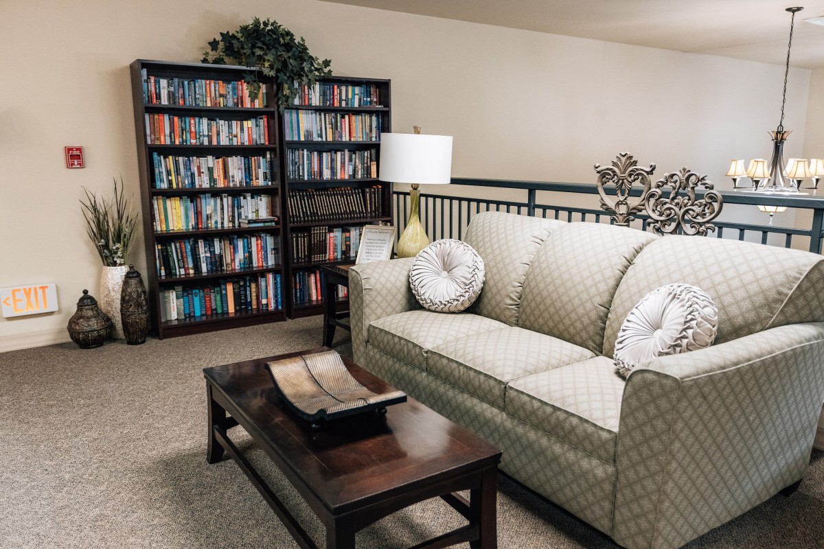 A cozy living room featuring a bookshelf, a comfortable sofa with cushions, a coffee table, and a lamp.