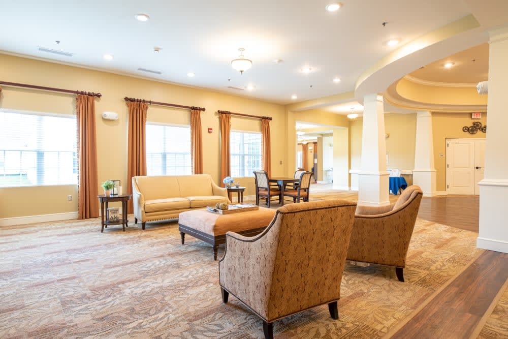 A spacious and well-lit living room featuring comfortable seating, a central table, and large windows with curtains.