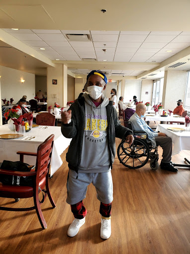 A person in a mask dances in a community dining area while others enjoy their time.