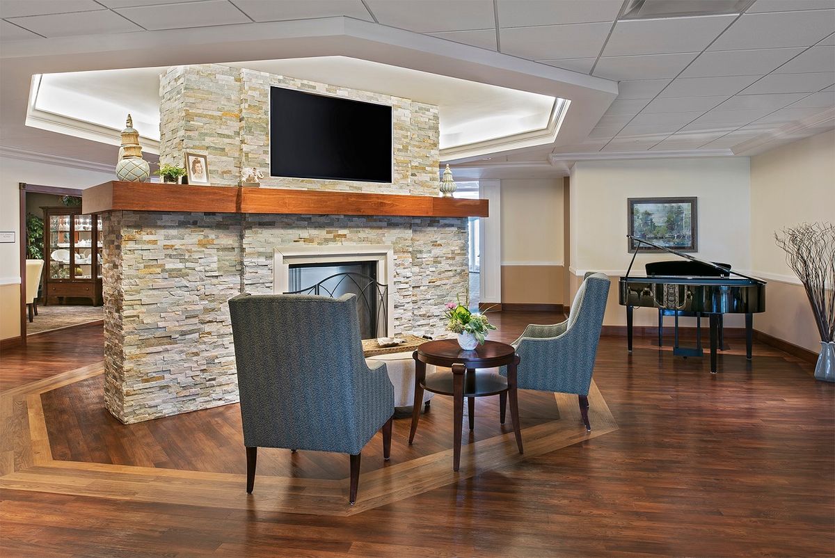 A modern living room with a stone fireplace, two armchairs, a small coffee table, and a TV mounted above the mantle.