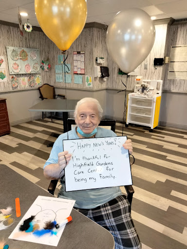 A joyful birthday celebration with an elderly person holding a sign, surrounded by festive decorations and balloons.