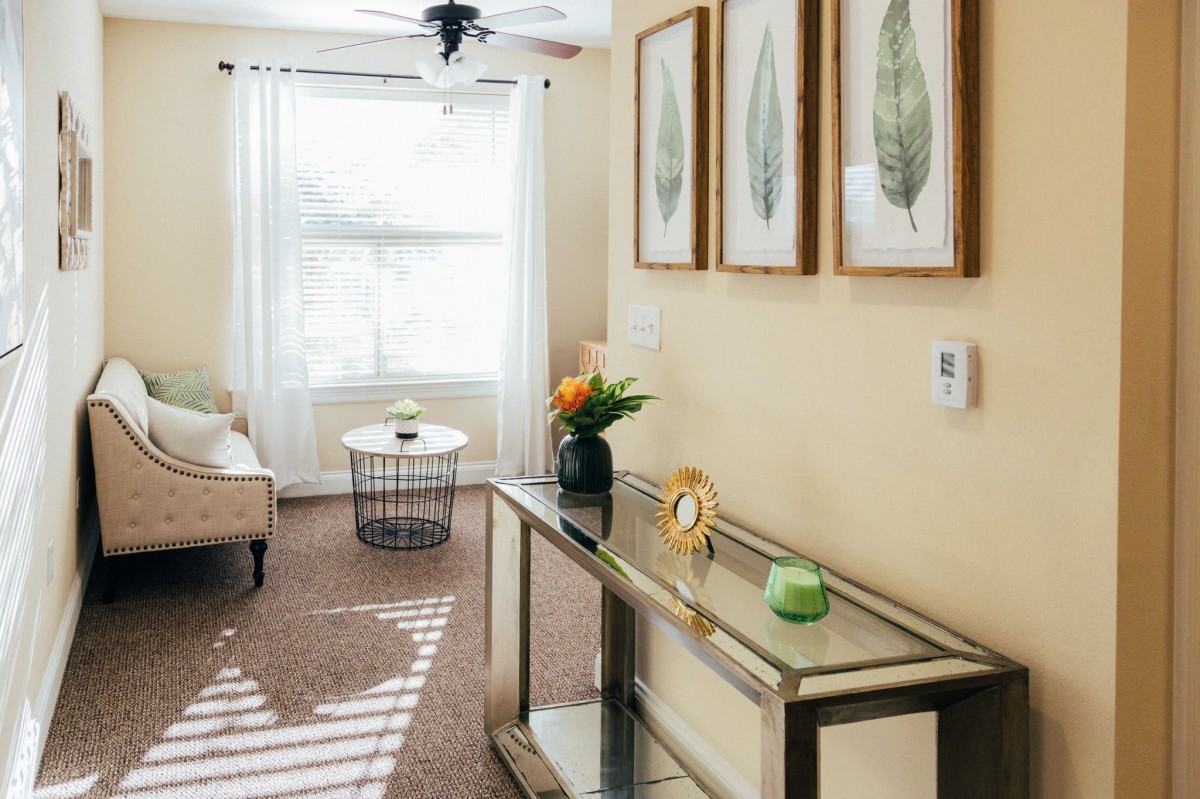 A cozy living room with modern decor, featuring a glass console table and framed botanical artwork.