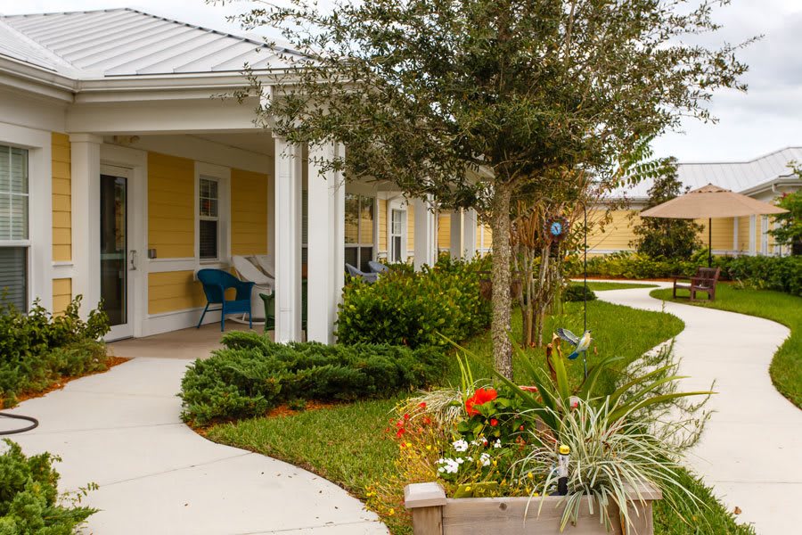 A cozy house with a porch, surrounded by a well-maintained garden and trees.