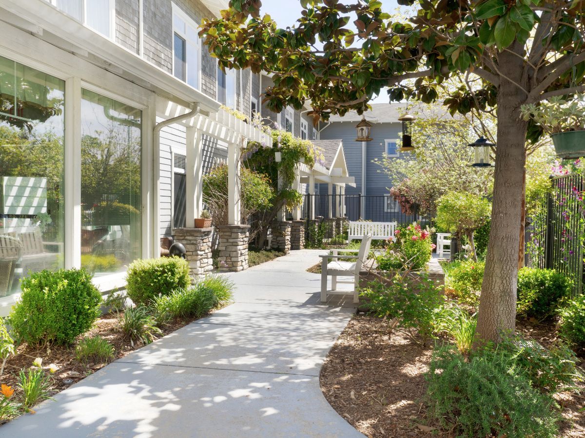 A peaceful garden pathway with benches and surrounding greenery next to a building.