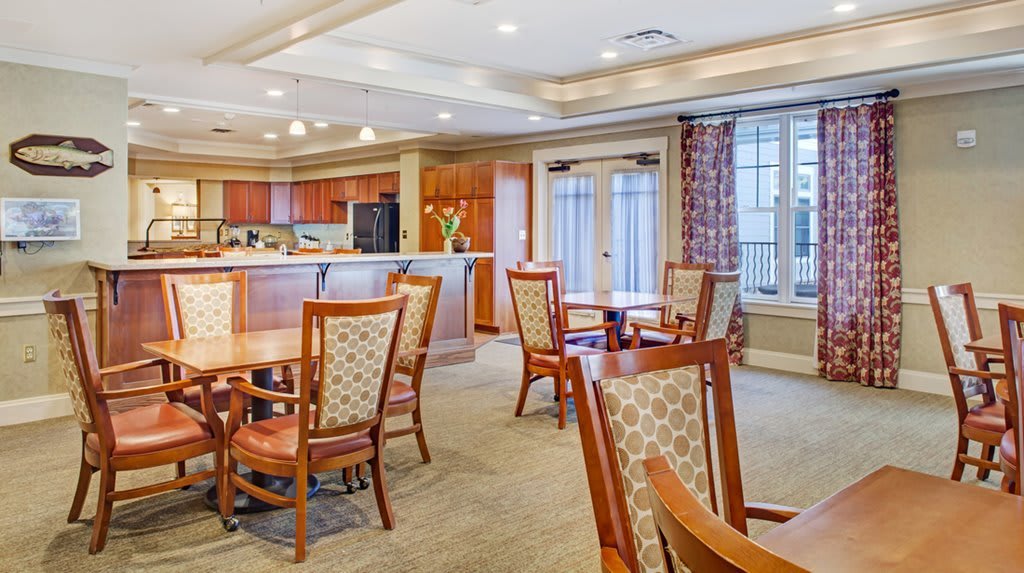 A spacious dining area with wooden tables and chairs, featuring large windows and warm lighting.
