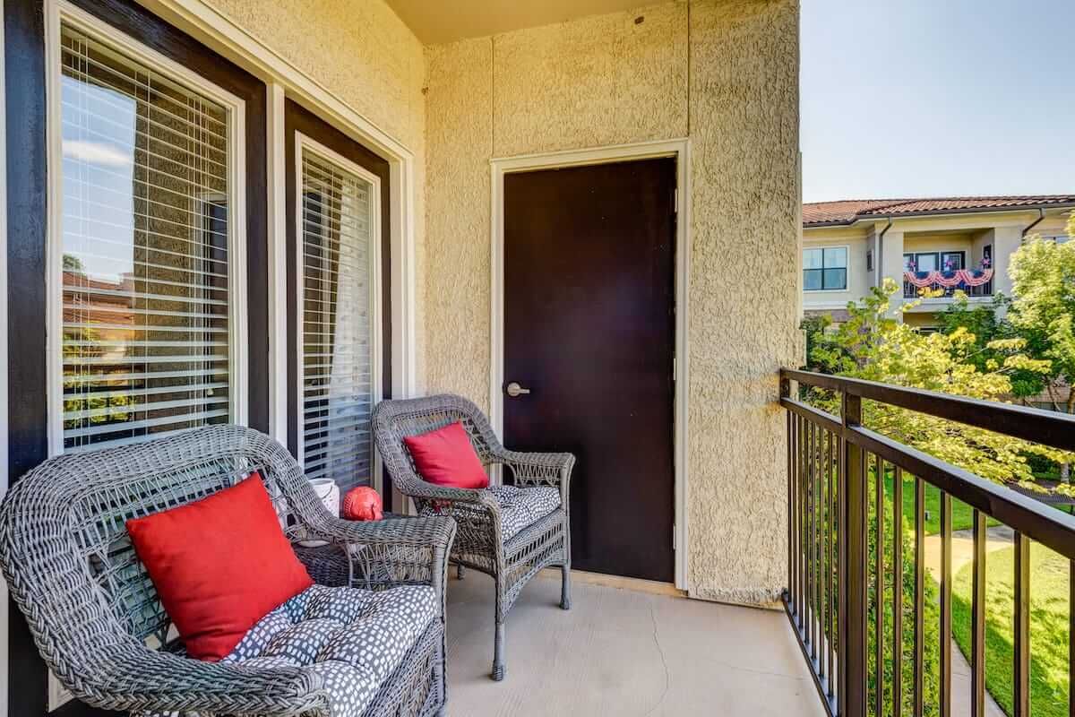 Cozy apartment balcony with wicker chairs and red cushions.