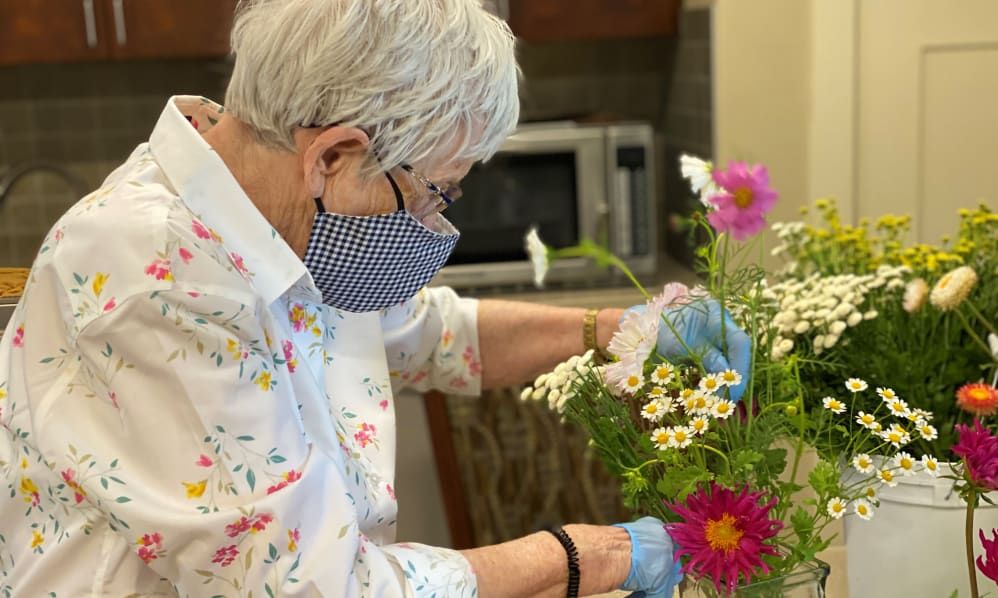An older adult arranges a bouquet of flowers while wearing a mask indoors.