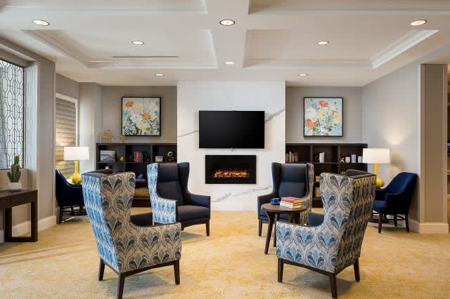 A cozy living room with patterned chairs around a modern fireplace and TV, featuring decorative artwork.