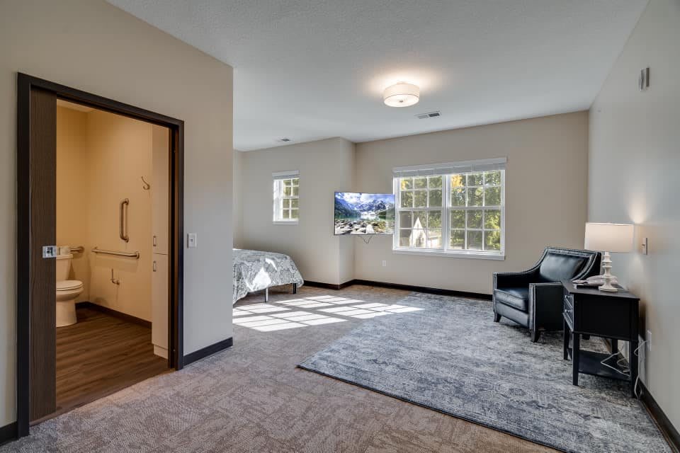 Spacious bedroom with a bed, armchair, and wall-mounted TV.