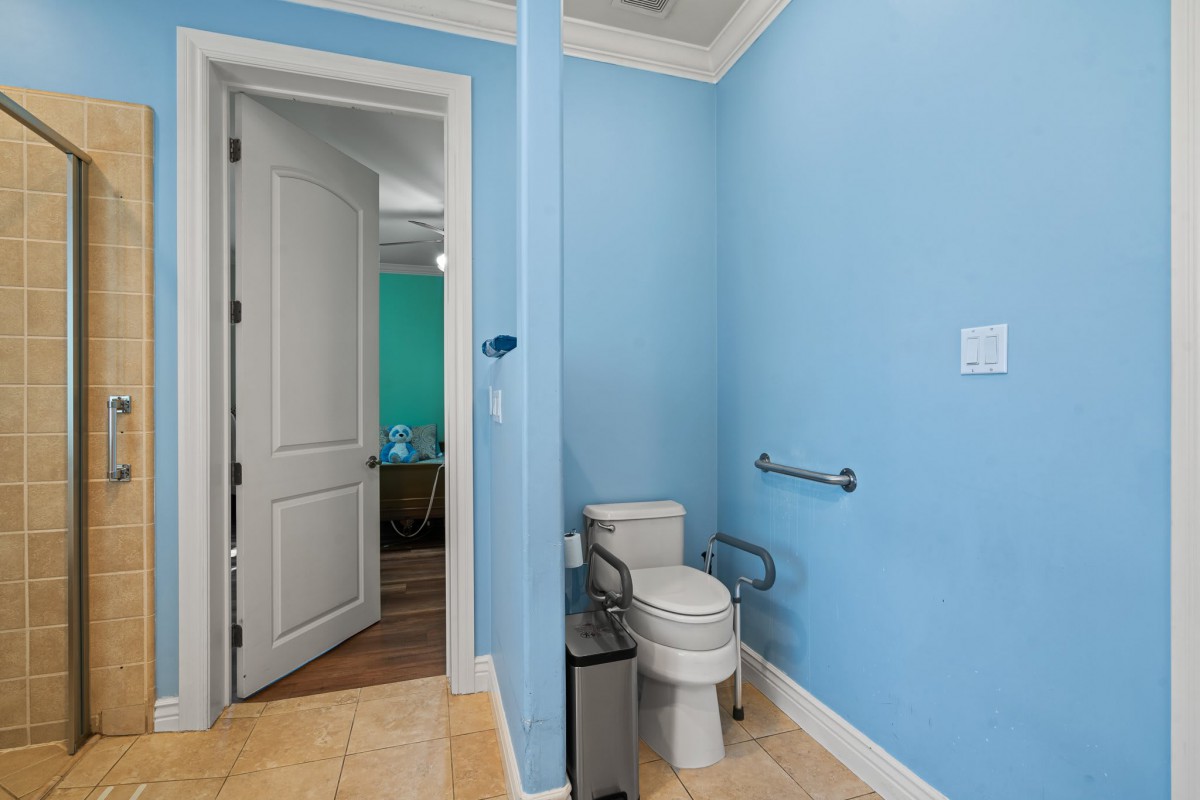 A bathroom featuring blue walls and a toilet with a wall grab bar, visible through an open door.