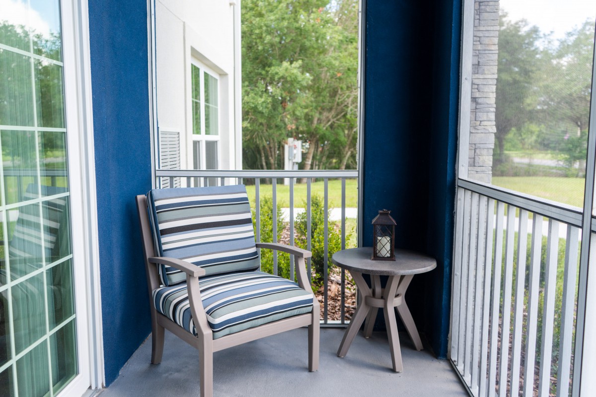 A cozy balcony setup with a striped cushioned chair and a small table featuring an outdoor lantern.