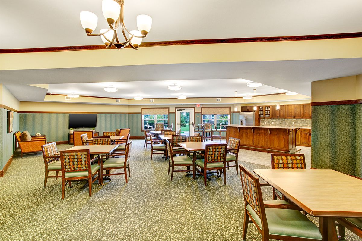 A spacious and well-lit dining area featuring wooden tables and chairs, illuminated by an elegant chandelier.