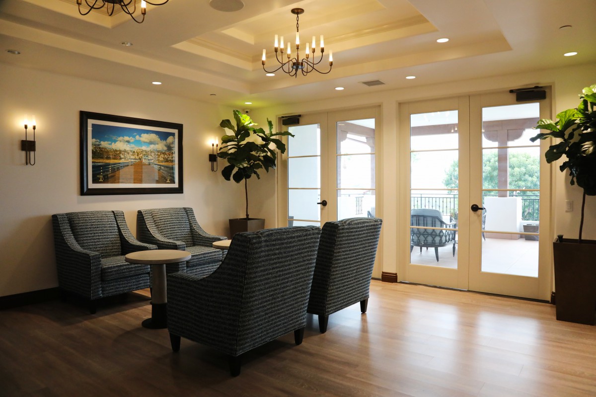 A cozy living room with elegant chandeliers, comfortable seating, and large glass doors leading to a balcony.