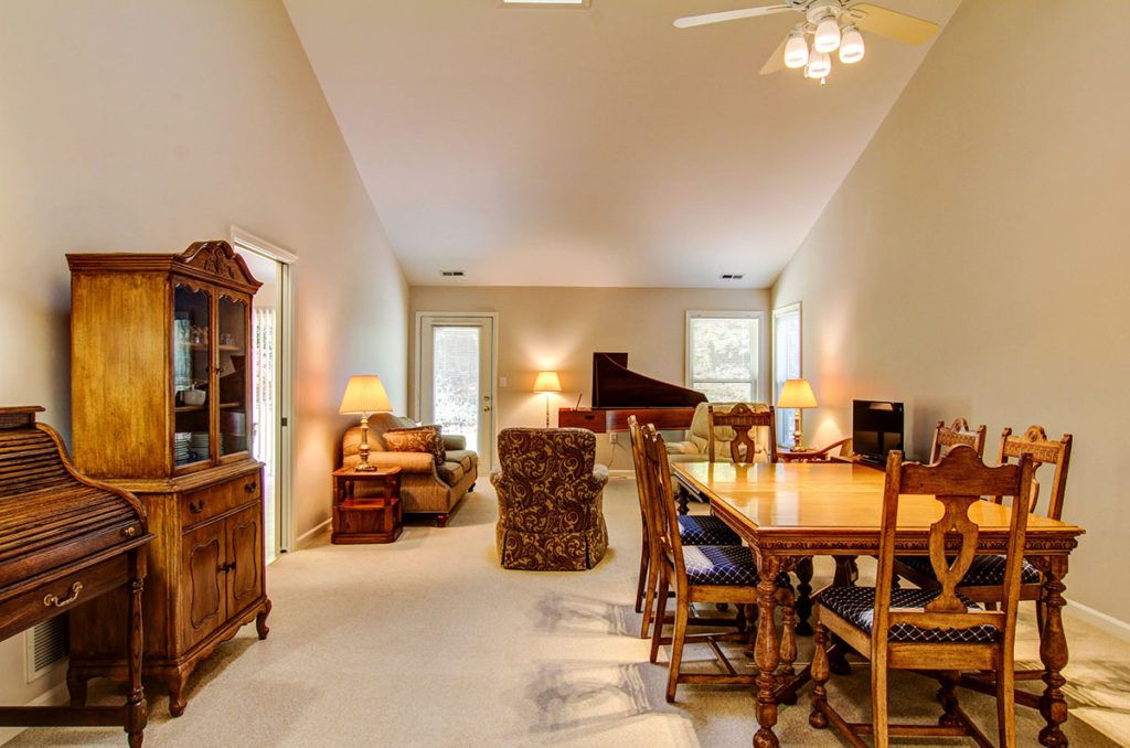 A spacious living and dining area featuring a grand piano, dining table with chairs, and elegant decor.