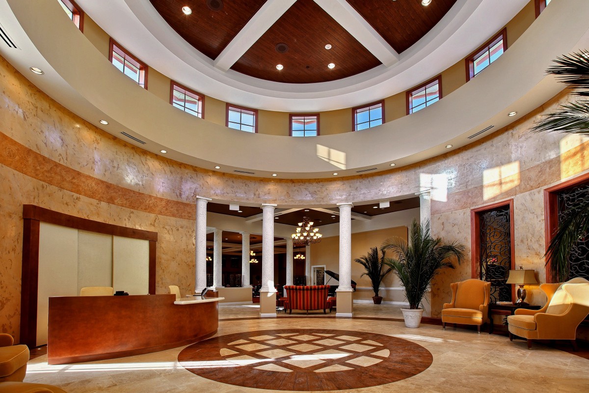 A spacious and modern lobby with elegant architecture, featuring a central reception desk, columns, and a decorative ceiling.