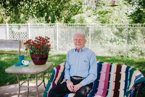 An elderly man enjoying a sunny day outdoors, seated on a colorful blanket with vibrant flowers nearby.