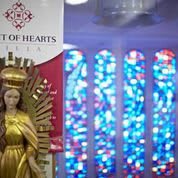 A statue of a religious figure is displayed beside vibrant stained glass windows in a church setting.