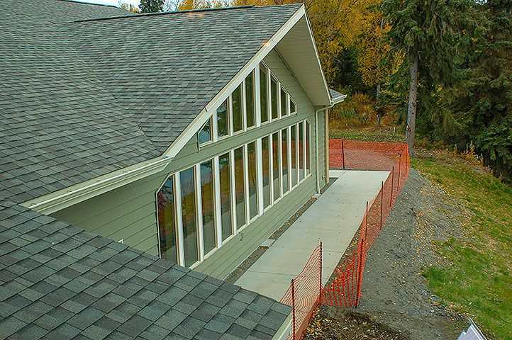 A newly constructed house with large windows and a sloped roof, surrounded by autumn trees.