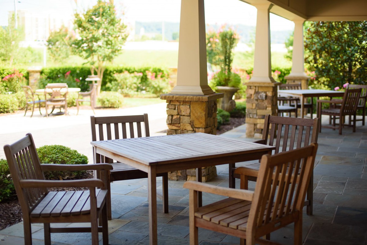 A sunny outdoor patio with wooden tables and chairs set in a garden.