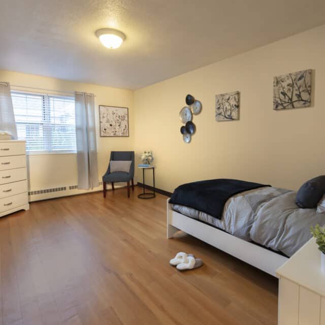 A minimalist bedroom with a single bed, hardwood flooring, and decorated walls.