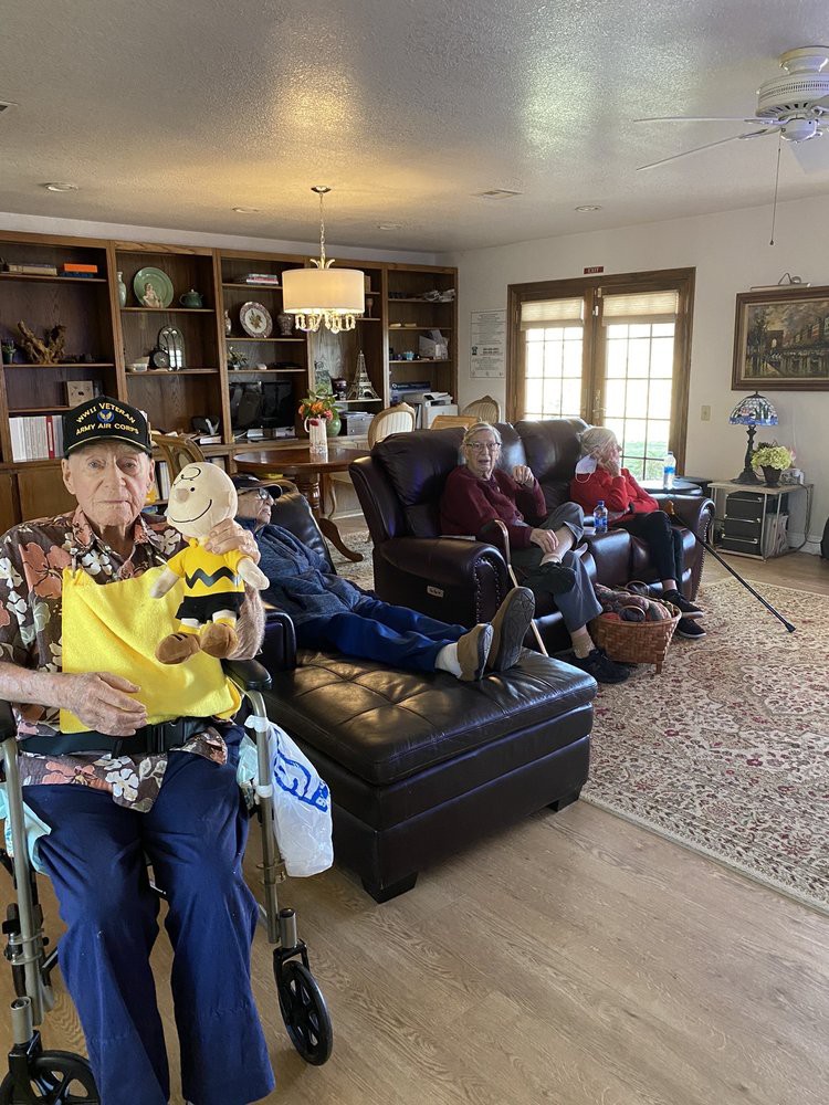 A group of seniors relaxing in a living room, one holding a plush toy.