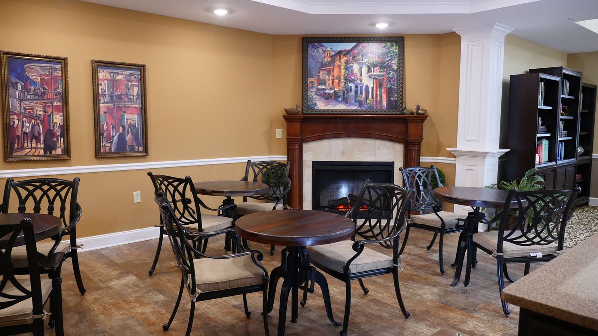A cozy cafe seating area with round tables and wrought iron chairs, featuring a fireplace and paintings on the walls.