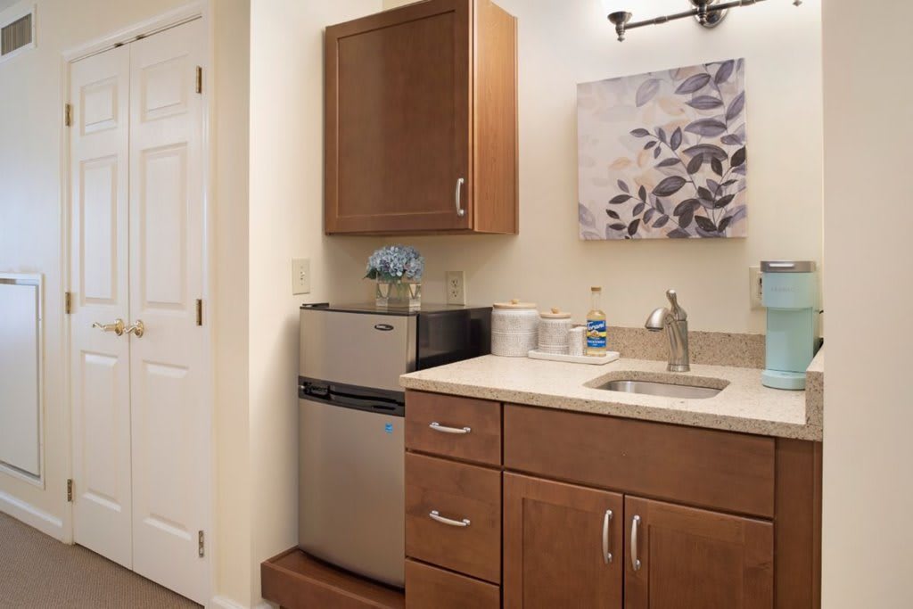 A compact kitchenette with wooden cabinets, a mini fridge, and a small sink.